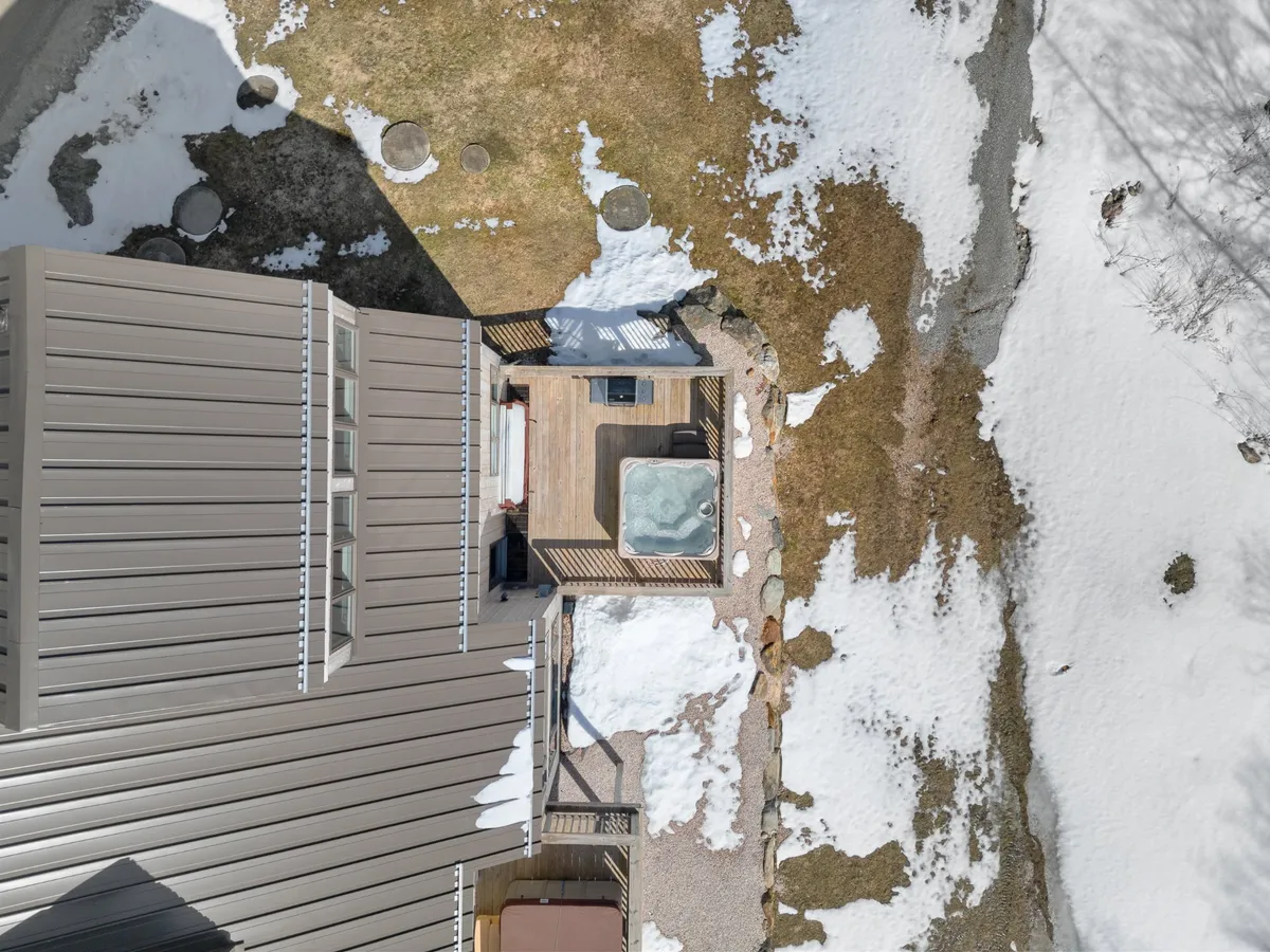 An outdoor jacuzzi and spacious deck surrounded by snow and landscaping. The setting feels tranquil and versatile, suitable for both winter evenings and sunny afternoons with friends and family, reinforcing the multi-season appeal.