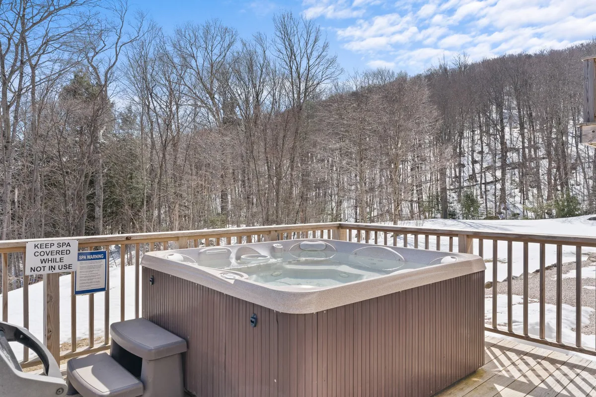 A peaceful exterior winter scene showcases a hot tub surrounded by snow-laden trees and a deck railing, evoking the essence of an intimate mountain wellness retreat. The environment is calm and naturally beautiful, ideal for unwinding after adventure-filled days on the slopes. The placement of the hot tub under open skies makes it perfect for stargazing, reinforcing the romantic angle of the section.