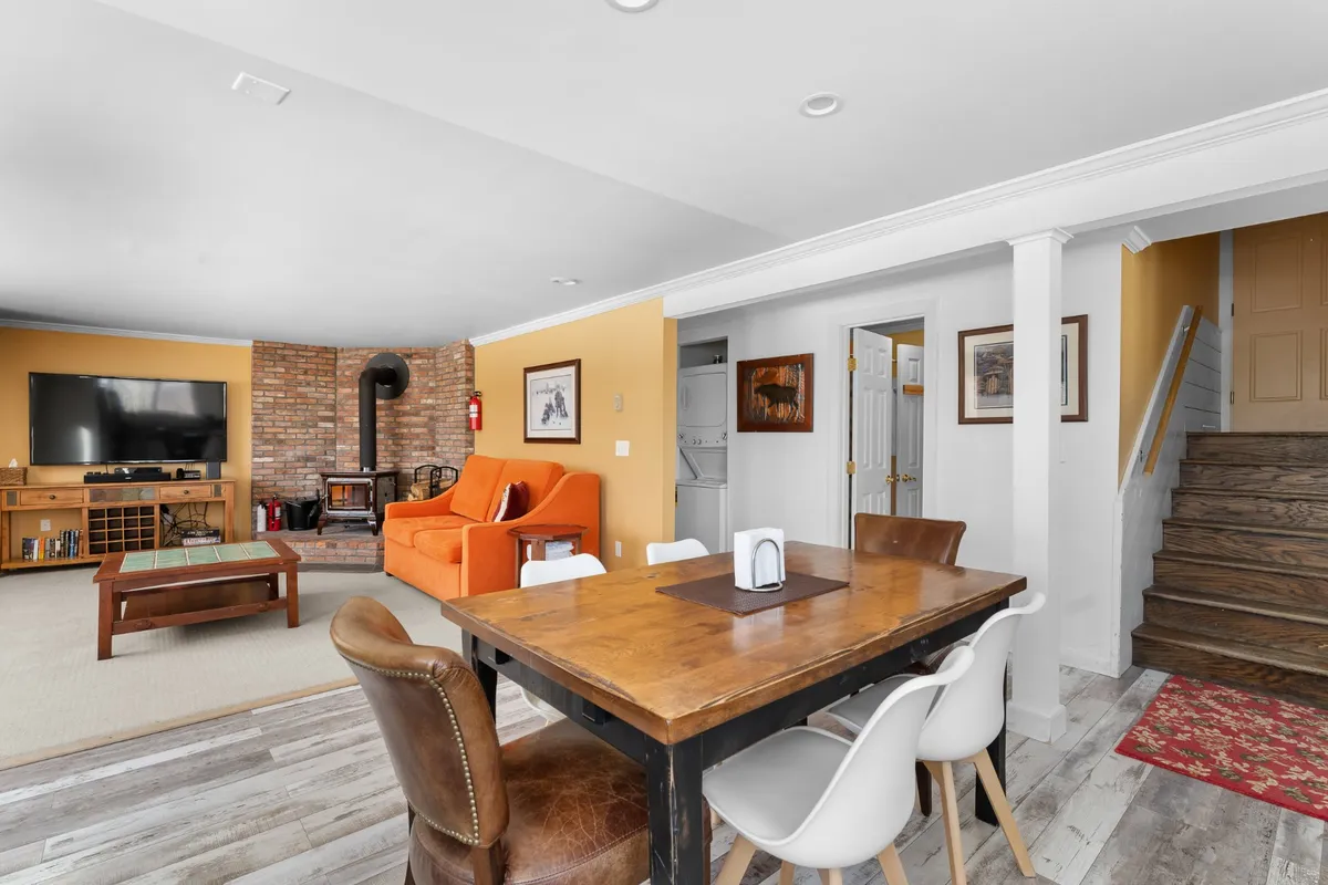 A cozy living area featuring an orange sofa, dining table, brick fireplace, and a television. The space is set up for relaxation and entertainment, illustrating where guests can enjoy high-speed Wi-Fi, streaming, and unwind in safety and comfort.