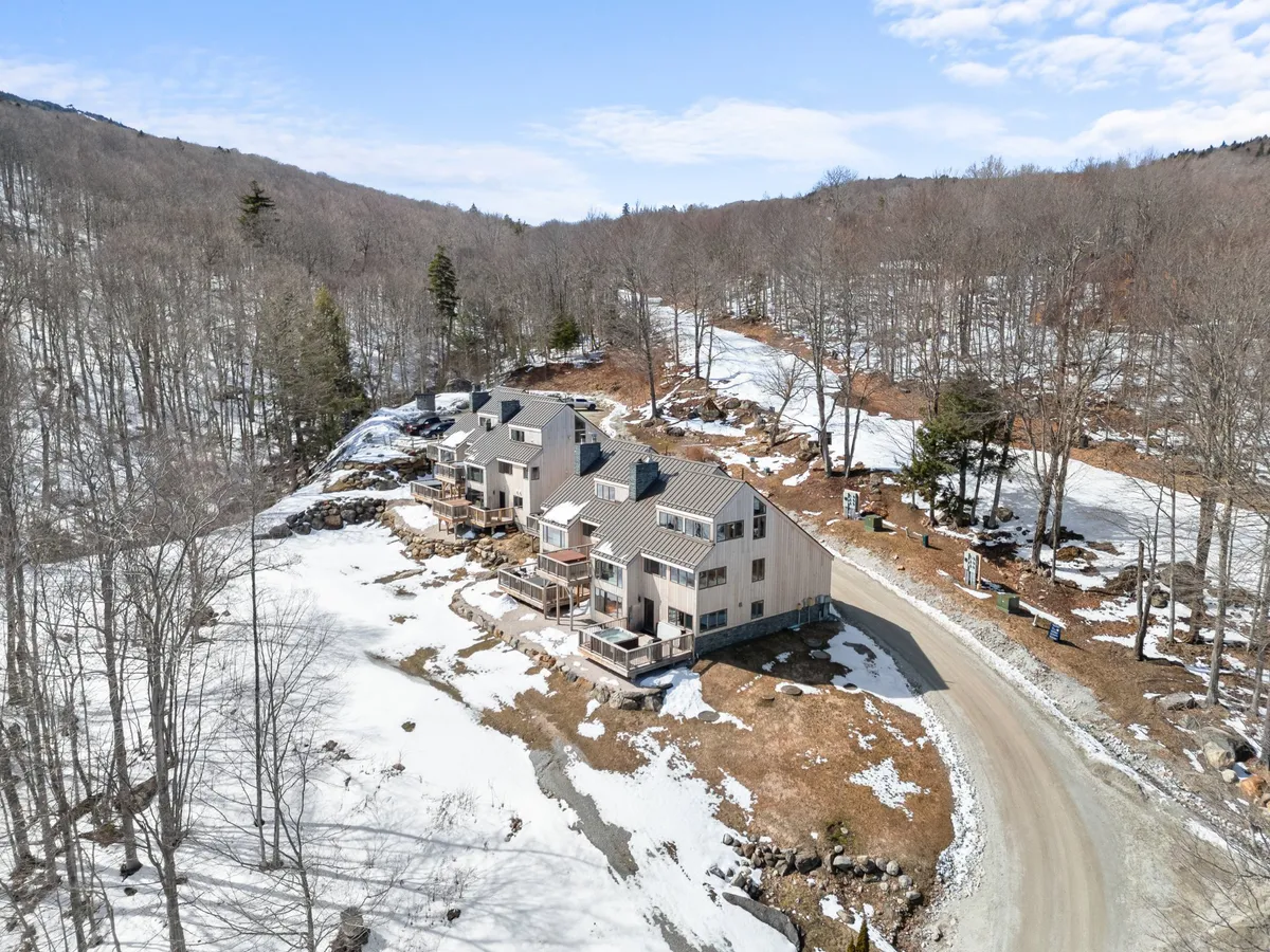 A row of charming houses sits amid a peaceful, snow-covered landscape, with a dirt road suggesting easy connectivity and community. The surroundings evoke tranquility and the spirit of winter recreation, making it clear that skiing and snowboarding are right outside.