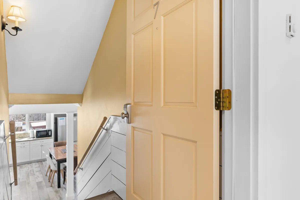 The photo captures a bright entryway with a yellow front door, stairs, and a glimpse of the kitchen area beyond. The scene evokes the moment of entering the home, hinting at both the welcoming atmosphere and the integrated technology that supports a comfortable stay.