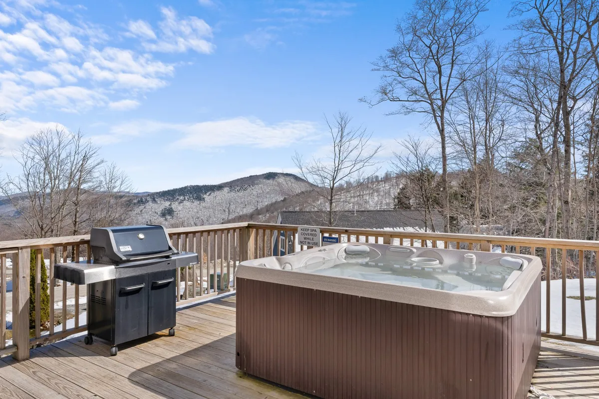 A private deck equipped with a hot tub and a BBQ grill overlooks the mountains, surrounded by natural beauty. The inviting outdoor space promises both relaxation and al fresco dining with a stunning view.