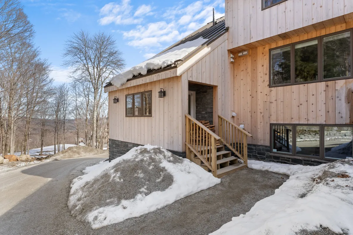 This inviting exterior image shows the property’s wooden staircase, a robust stone foundation, and large windows, all dusted with fresh snow. The porch offers a cozy setting for starry nights or quiet evenings after outdoor adventure. The welcoming mood and architectural elements highlight the condo’s unique, private mountain character, setting the stage for romantic evenings both inside and out.