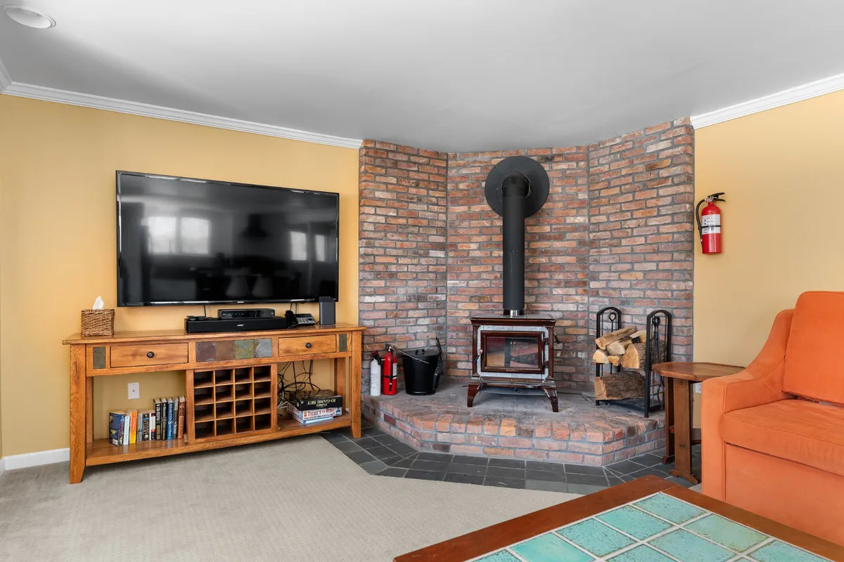A close-up view of the living area's wood stove and TV, accented by a plush orange chair and wooden cabinet. The space exudes warmth and comfort, ideal for unwinding, reading, or enjoying a movie night after outdoor adventures.