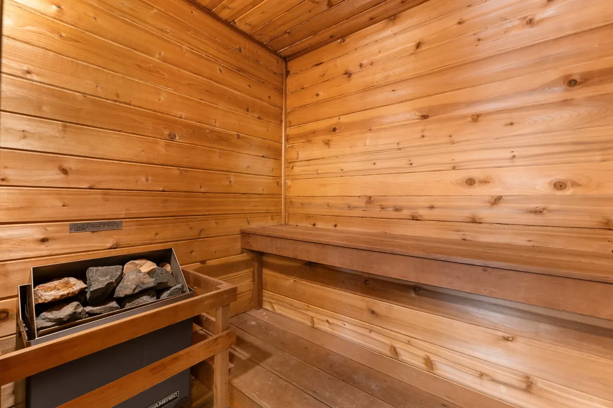 A cedar sauna with wooden benches and a stone heater, surrounded by warm wood paneling. The scene evokes relaxation and a spa-like retreat, highlighting the property’s unique wellness amenity.