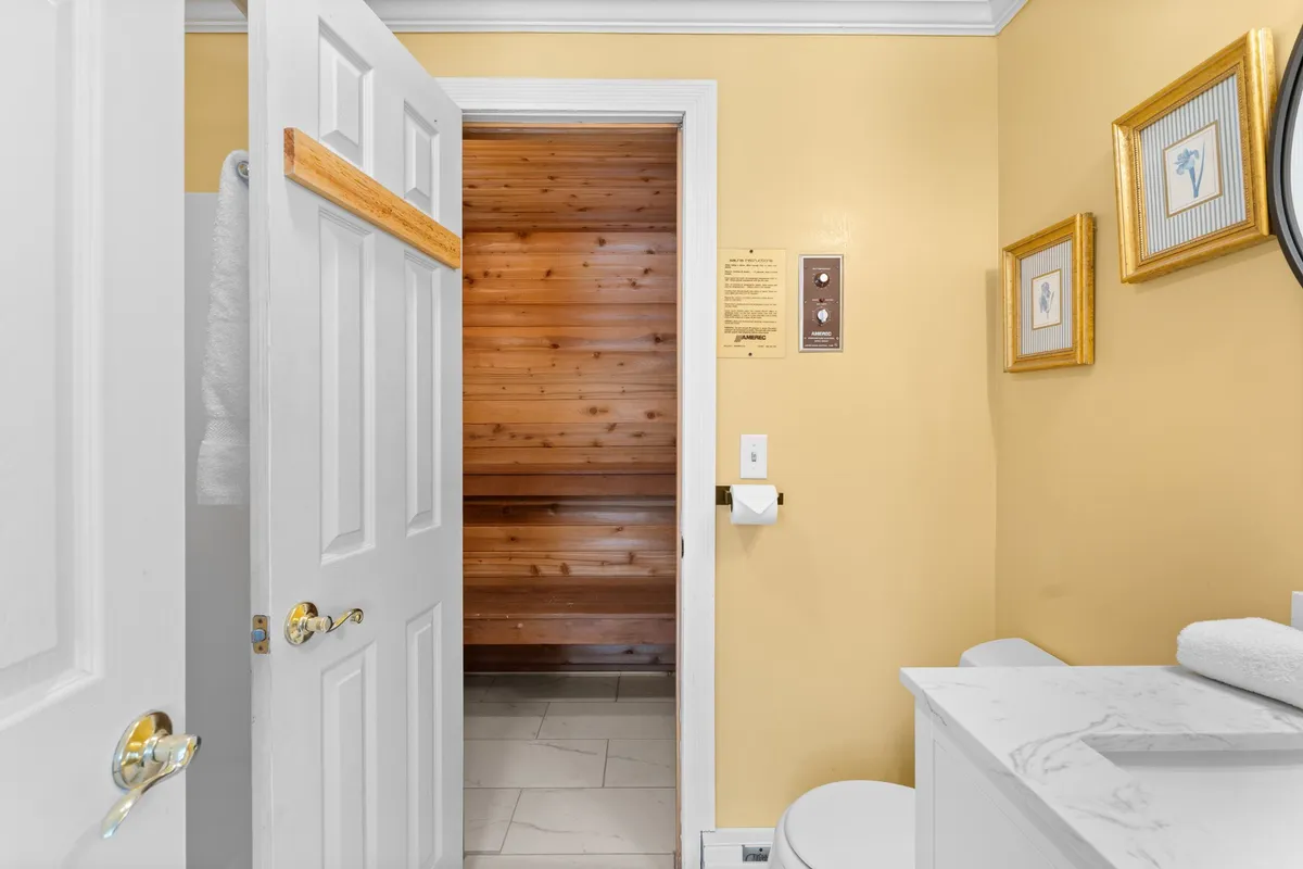 The image displays the entrance to a sauna, decorative artwork, a modern vanity with sink, and towels neatly arranged. The room feels serene and organized, suggesting a comfortable transition between bathing and sauna experiences.